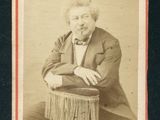 portrait d'un homme en costume et nœud papillon, assis sur une chaise