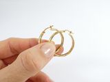 a person holding a pair of gold hoop earrings