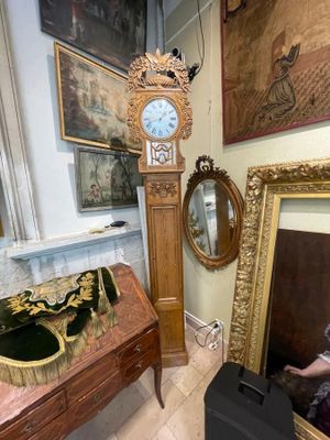 une horloge de parquet dans un coin d'une pièce où sont accrochés des tableaux au mur
