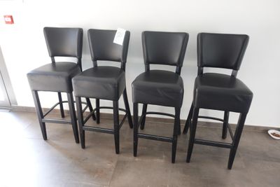 quatre tabourets de bar en cuir noir disposés devant un mur blanc