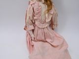 poupée assise par terre, vêtue d'une robe rose et d'un chapeau