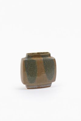 un petit vase marron et vert posé sur une surface blanche
