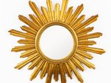 un miroir doré en forme de soleil rayonnant accroché à un mur blanc