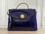blue leather handbag with golden buckle on wooden table in front of white wall