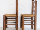 pair of wooden chairs with rattan seats against a white wall