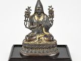 a bronze figure of a seated buddha on a wooden base