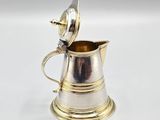 a silver plated pitcher with a lid on a white surface