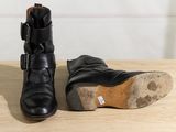 pair of black leather boots with buckles sitting on a wooden table