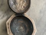 une petite boîte en argent avec un couvercle en argent, posée sur une table