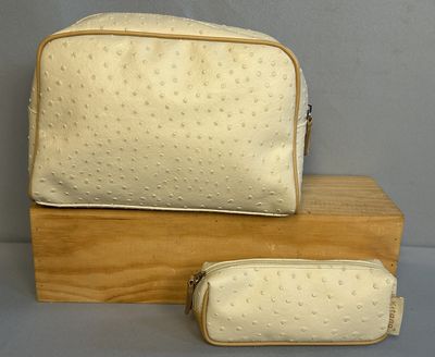 Trousse de maquillage et trousse à crayons en autruche beige, posées sur un support en bois