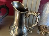 un pichet en argent posé sur une étagère à côté d'autres objets en argent
