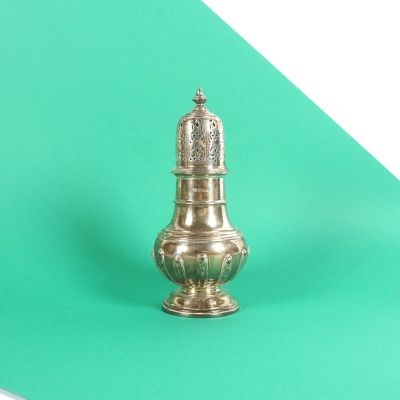 une salière en argent posée sur une surface verte