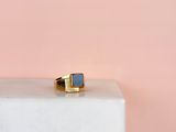 une bague en or et pierre bleue posée sur un bloc de marbre