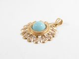 a close up of a gold pendant with a turquoise stone