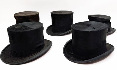 Plusieurs chapeaux-hauts noirs sont alignés en rang sur une surface blanche