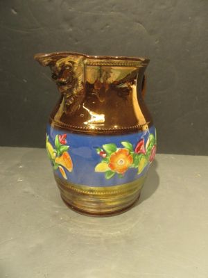 a brown and blue vase with oranges on it on a table