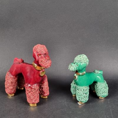 une paire de figurines de caniches rouges et verts posées sur un socle noir