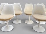 four white tulip chairs with beige cushions on a gray surface