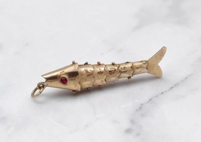 une image représentant un pendentif en forme de poisson rouge posé sur un plan de travail en marbre