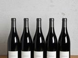six bottles of red wine lined up on a wooden table
