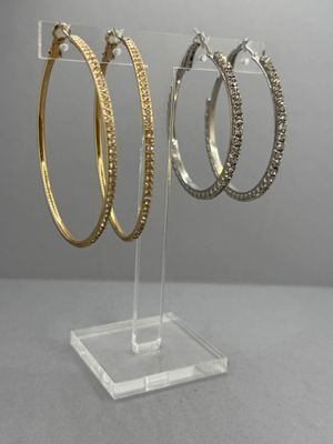 trois paires de boucles d'oreilles créoles en or et en argent, présentées sur un présentoir en acrylique transparent