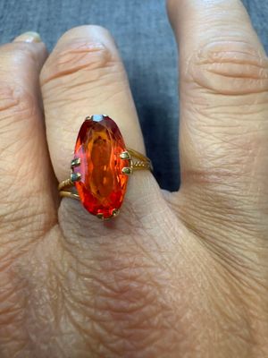 une image représentant la main d'une femme tenant une bague sertie d'une pierre orange