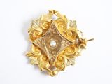 une image d'une broche en or avec une perle au centre