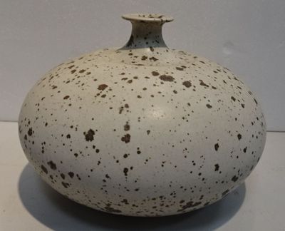 un vase blanc parsemé de taches marron, posé sur une table
