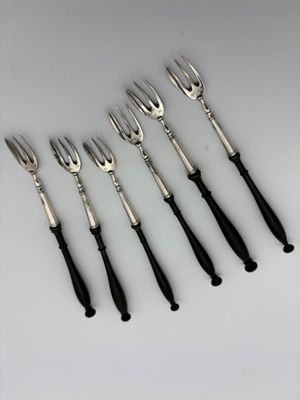 six forks and a knife are lined up on a white surface