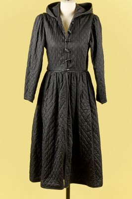 un manteau noir posé sur un pied de mannequin, devant un fond jaune
