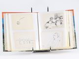 un livre ouvert, orné de dessins, posé sur une surface blanche