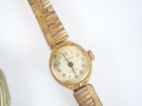 a gold watch sitting on a white surface next to a bottle