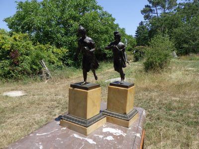 deux statues en bronze représentant un homme et une femme, posées sur des socles