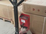 des cartons empilés sur des palettes dans un entrepôt, avec un diable au premier plan
