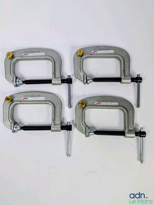 quatre colliers métalliques fixés sur une surface blanche à l'aide de vis et d'écrous