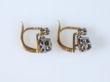 une paire de boucles d'oreilles en or et diamants posées sur une surface blanche