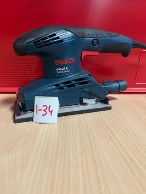 un gros plan d'une ponceuse Bosch posée sur une table, à côté d'une boîte rouge