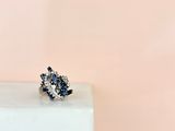 a close up of a diamond and sapphire cluster ring on a white marble block