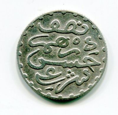 une vieille pièce de monnaie portant une inscription en arabe, posée sur une surface blanche