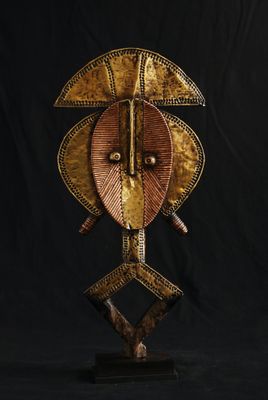 une sculpture représentant un masque africain posée sur un socle, sur fond noir