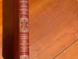 a red book sitting on a wooden floor next to a clock