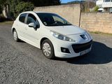 La petite voiture blanche est garée sur le gravier, près d'un mur de briques.