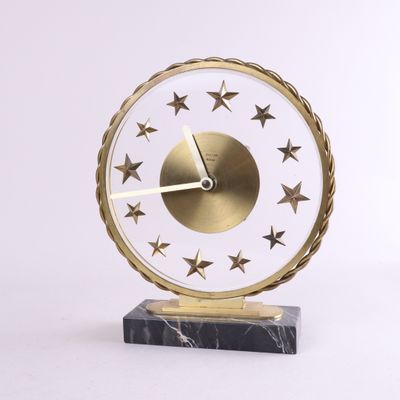 horloge dorée et blanche ornée d'étoiles, posée sur un socle en marbre, sur fond blanc