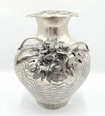 a silver vase with flowers on it sitting on a table