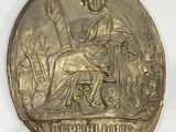 gold medal with a woman seated on a bench in a garden