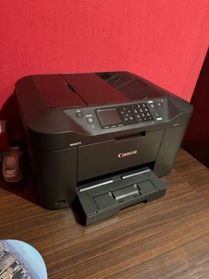 une imprimante Canon posée sur une table en bois, près d'un mur rouge