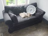 un chat allongé sur un canapé sur lequel se trouve une horloge