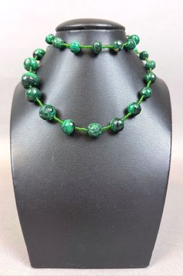 a close up of a necklace with green beads on a mannequin