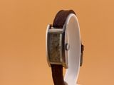 une image représentant une montre posée sur un socle, sur un fond marron