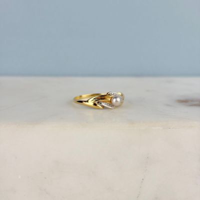 bague en or jaune ornée d'une perle et de diamants, posée sur une plaque de marbre